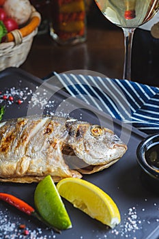 Grilled fish on a plate with a glass of wine and baked vegetables.