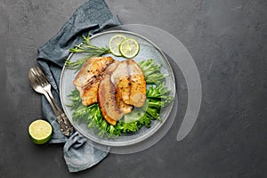 Grilled fish sea bass fillet with green lettuce in a plate on a black stone background