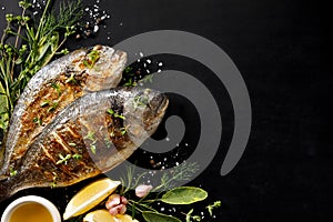 Grilled fish, sea bream with additions, herbs, olive oil, spices on a black background. Composition in the bottom left corner