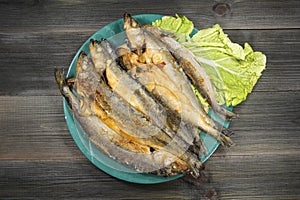 Grilled fish - smelt on a plate with green salad on an old black wooden background