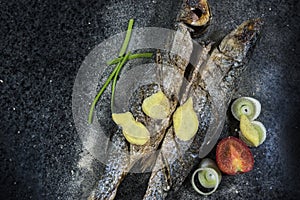 Grilled fish with spices, vegetables and herbs on slate background ready for eating.