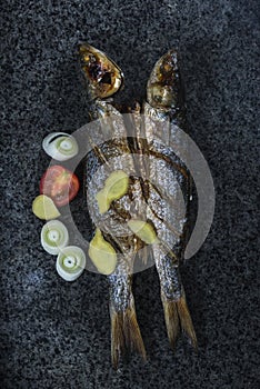 Grilled fish with spices, vegetables and herbs on slate background ready for eating.