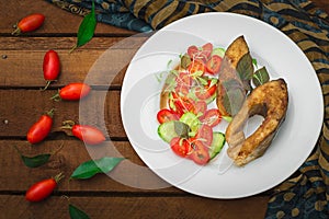 Grilled fish steak with vegetables on plate: tomatoes, microgran, cucumber, tasty and healthy dinner. Wooden rustic background. To