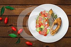 Grilled fish steak with vegetables on plate: tomatoes, microgran, cucumber, tasty and healthy dinner. Wooden rustic background. To