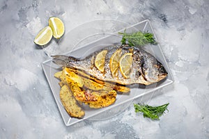 Grilled fish on stone plate with lemon on concrete background