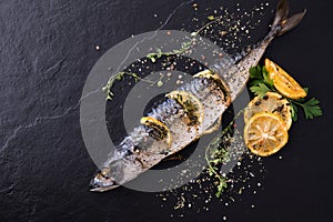 Grilled fish and various vegetables on black stone background