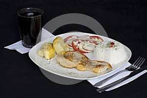 Grilled fish and vegetables, potatoes, rice, tomatoes and a glass of chicha.