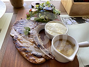 Grilled or fried pork chops on the bone with salad and mashed potatoes served on wooden board