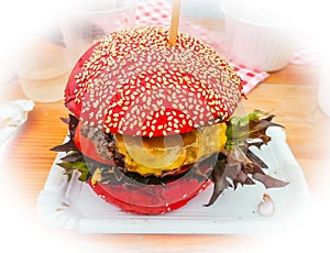 Grilled gamburger on picnic desk with red bun.