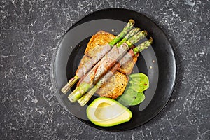 Grilled green asparagus wrapped with bacon and avocado on toasts