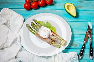 Grilled green asparagus wrapped with bacon, benedict poached egg on blue wood background