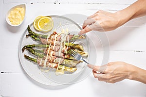 Grilled green asparagus wrapped with bacon. Female hands holds knife and fork. Ketogenic diet. Healthy food