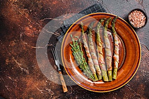 Grilled green asparagus wrapped with bacon on a plate. Dark background. Top view. Copy space