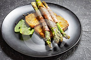 Grilled green asparagus wrapped with bacon on toasts