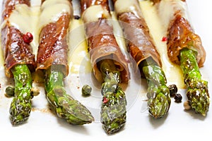 Grilled green asparagus wrapped in prosciutto bacon on a white b