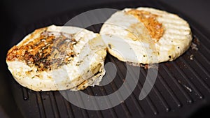 grilled haloumi cheese is grilled on a dark metal grill pan in close - up.