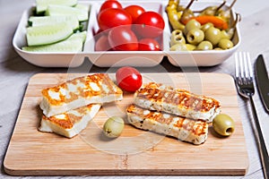 Grilled haloumi cheese on a wooden board with olives, cherry, cucumbers and pepperoni