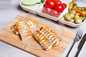 Grilled haloumi cheese on a wooden board with olives, cherry, cucumbers and pepperoni