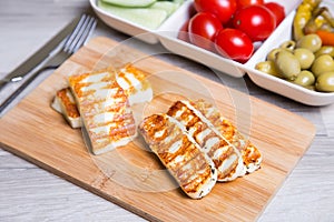 Grilled haloumi cheese on a wooden board with olives, cherry, cucumbers and pepperoni photo