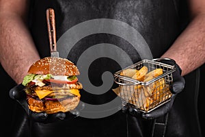 Grilled hamburger with meat cutlet and fries in hands. Fast food concept. Burger and fries
