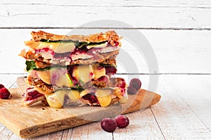 Grilled holiday turkey, cranberry and brie sandwich stack against a white wood background