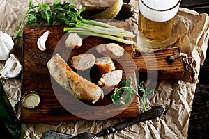 Grilled homemade sausage meat on a cutting board, onion, garlic, pickles and beer, fork and knife on paper