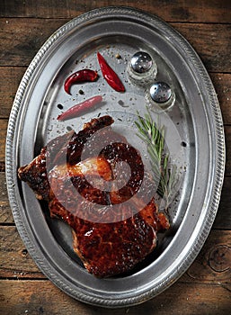 Grilled juicy beef steak with rosemary, salt, pepper and chili pepper on an iron plate on the wooden table