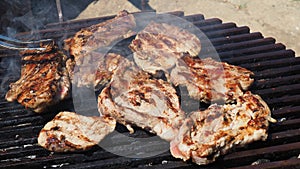 Grilled juicy meat pork steaks in burning coals on a barbecue grill, white smoke. Crispy crust. Tasty steak with blood and fried