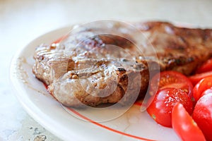 Grilled juicy pork meat steak with vegetables cherry tomatoes on a white plate