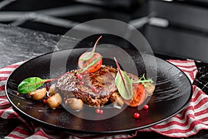 Grilled juicy steak with grilled mushrooms, tomatoes and cranberries on a dark plate and rad napkin on a dark background