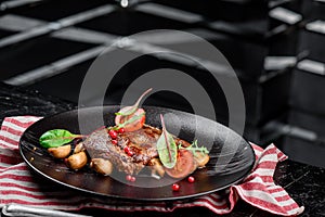 Grilled juicy steak with grilled mushrooms, tomatoes and cranberries on a dark plate and rad napkin on a dark background
