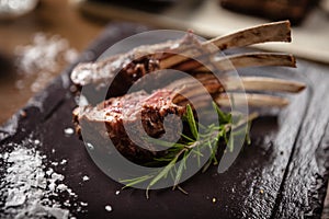 Grilled lamb chops with a branch of rosemary on a black board. Delicious healthy gourmet meat food closup served for