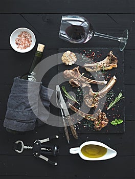 Grilled lamb chops. Rack of Lamb with garlic, rosemary, spices on slate tray, wine glass, oil in a saucer and bottle