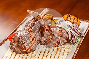 Grilled lamb chops served with flatbread, grilled vegetables, and fresh onion salad on a rustic ceramic platter
