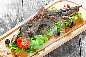 Grilled lamb ribs in herbs and greens, fresh salad, grilled vegetables and berries on cutting board on wooden background