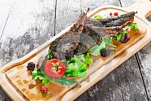 Grilled lamb ribs in herbs and greens, fresh salad, grilled vegetables and berries on cutting board on wooden background