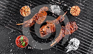 Grilled lamb ribs meat or rib eye with tomato sauce over the coals on a barbecue, dark background. Top view