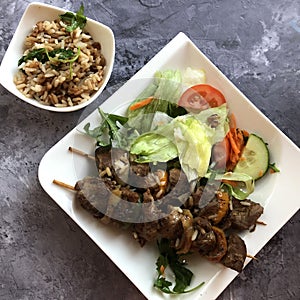 Grilled lamb on a skewer with rice, salad and fresh herbs.