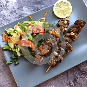 Grilled lamb on a skewer with salad and fresh herbs.