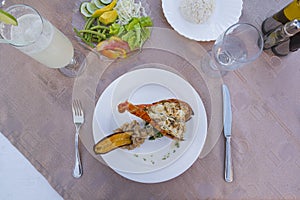 Grilled lobster is beautifully placed on a plate along with side dish of mashed potatoes, fried banana, vegetables and rice and a