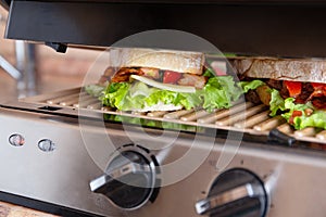 Grilled long sandwich or panini on the grill of an electric grill. Crisp bread, lettuce, tomato, cheddar, salsa sauce -