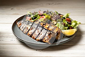 Grilled mackerel fillets with vegetables and lemon on blue plate in restaurant.