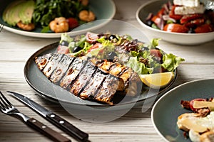 Grilled mackerel fillets with vegetables and lemon on blue plate in restaurant.