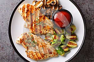 Grilled marinated healthy chicken breasts cooked on a summer barbecue and served with brussels sprouts and mushrooms close-up in a