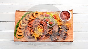 Grilled meat on the board. Sausage, ribs and fresh vegetables. On a wooden table.