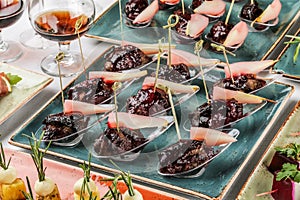 Grilled meat fillet canapes with baked pear and berry sauce in spoon on banquet table. Catering food, appetizer platter and snacks