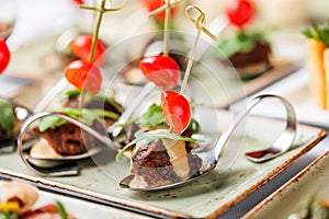 Grilled meat fillet canapes with cheese, tomatoes and greens in spoon on banquet table. Catering food, appetizer platter and