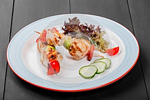 Grilled meat kebabs on skewers with vegetables, cherry tomato, pepper, zucchini in plate on dark wooden background.