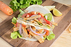 Grilled meat with onion and bell peppers, tomato,lettuce and serve with flour tortilla on wooden board.