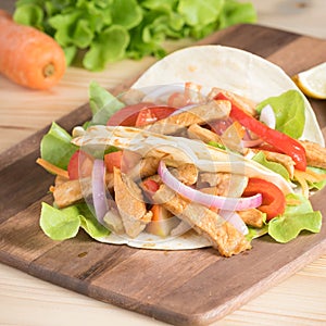 Grilled meat with onion and bell peppers, tomato,lettuce and serve with flour tortilla on wooden board.